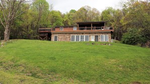 Une maison en pierre à deux étages, dotée d’une grande terrasse et d’un espace extérieur couvert.