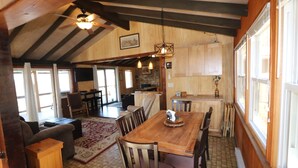 Un vaste espace dédié à la salle à manger, avec une table et des chaises en bois, un ventilateur de plafond et une vue sur la cuisine et le salon.