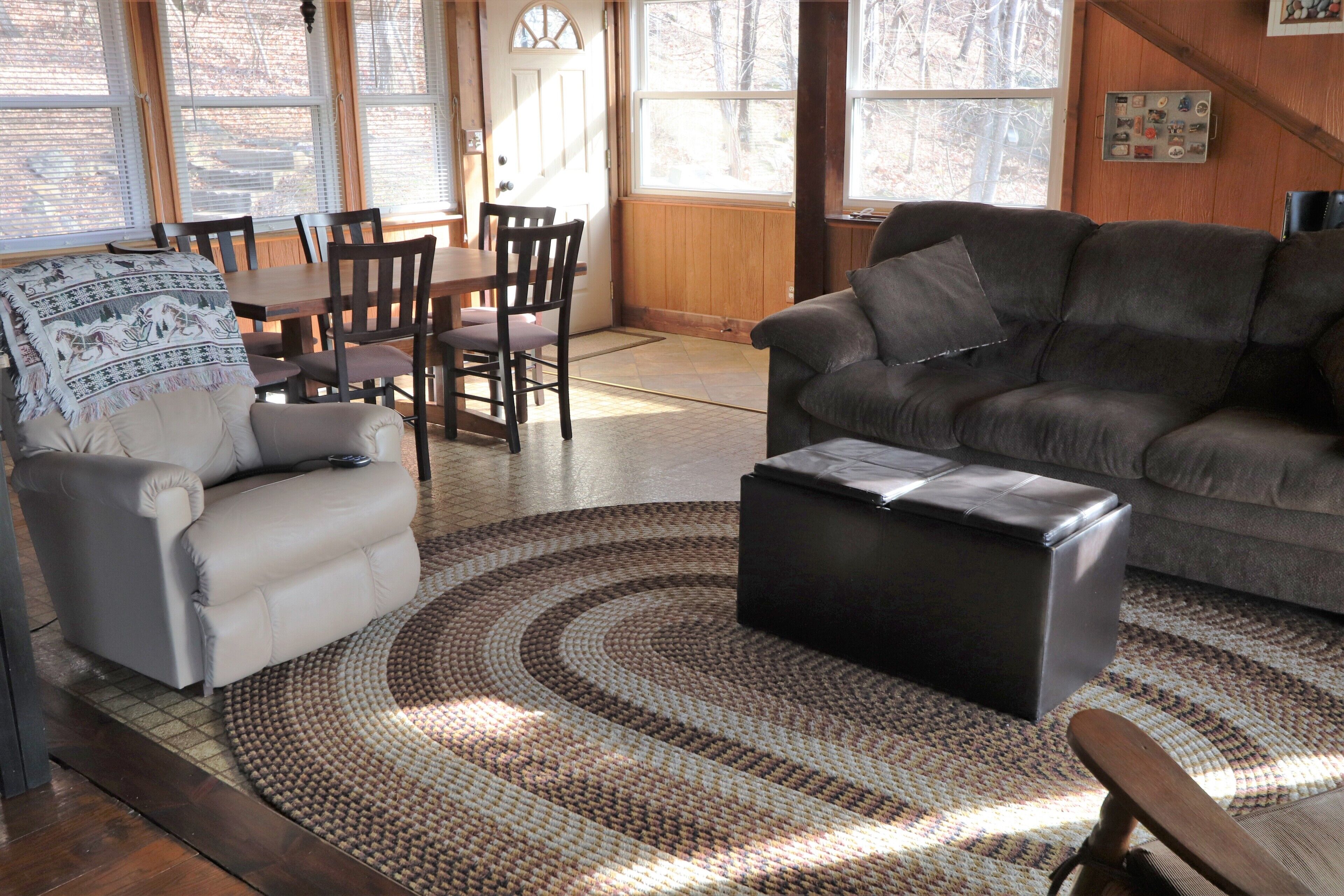Una sala de estar con un sofá gris, un tapete estampado y una zona de comedor con muebles de madera.