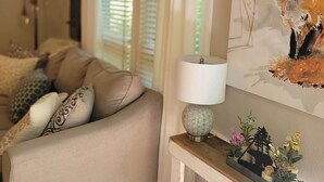 Een gezellige woonkamer met een bank, een lamp, een schilderij van een vos en een raam met jaloezieën.