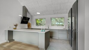 Uma cozinha moderna com uma ilha central, duas janelas com vista para o verde, e uma geladeira embutida.