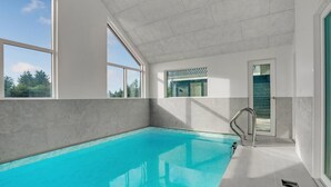 Piscina interior moderna com amplas janelas e vista para o exterior.