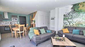 Una sala de estar moderna con un sofá gris, una mesa de comedor con sillas y una zona de cocina con estufa y horno.
