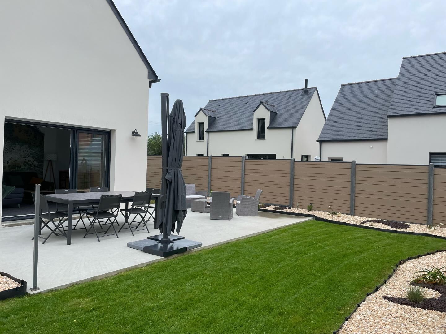 A modern house with a patio, a dining area, and a well-maintained lawn.
