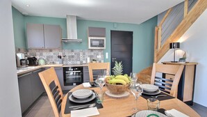 Une cuisine moderne avec un coin repas, comprenant une table en bois dressée pour quatre personnes, un panier de fruits et une porte noire.