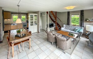 Eine moderne Küche mit Essbereich, ein Wohnzimmer mit Sofa und Sesseln sowie eine Treppe zu einer weiteren Ebene.