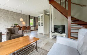 Relax in this spacious living room with a sofa, coffee table, and dining area, featuring a staircase leading to an upper level.