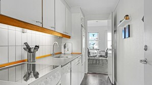 A modern kitchen with white cabinets, a stainless steel sink, and a built-in oven. - Cozy apartment in Rudkøbing (Rudkøbing)