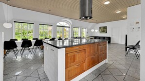 Een moderne keuken met een centraal eiland, grote ramen en een houten plafond.