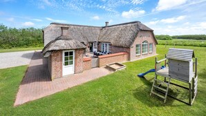 Een rieten huis met een bakstenen gevel, een terras en een speeltoestel.