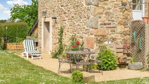 A stone building with a garden patio featuring a table and chairs, a wooden fence, and a variety of plants and flowers. - Stunning home in Pleudaniel (Pleudaniel)