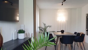 Un comedor moderno con una mesa larga, sillas negras y un televisor montado en la pared.
