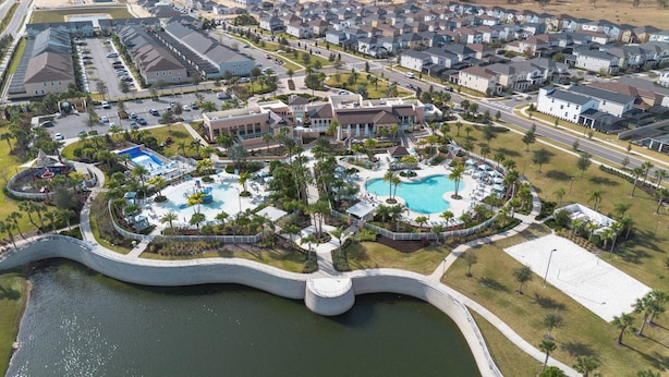 An aerial view of a residential area with a large swimming pool surrounded by palm trees and a bridge over a body of water. - 9BR house with private pool in Solara Resort (Kissimmee)