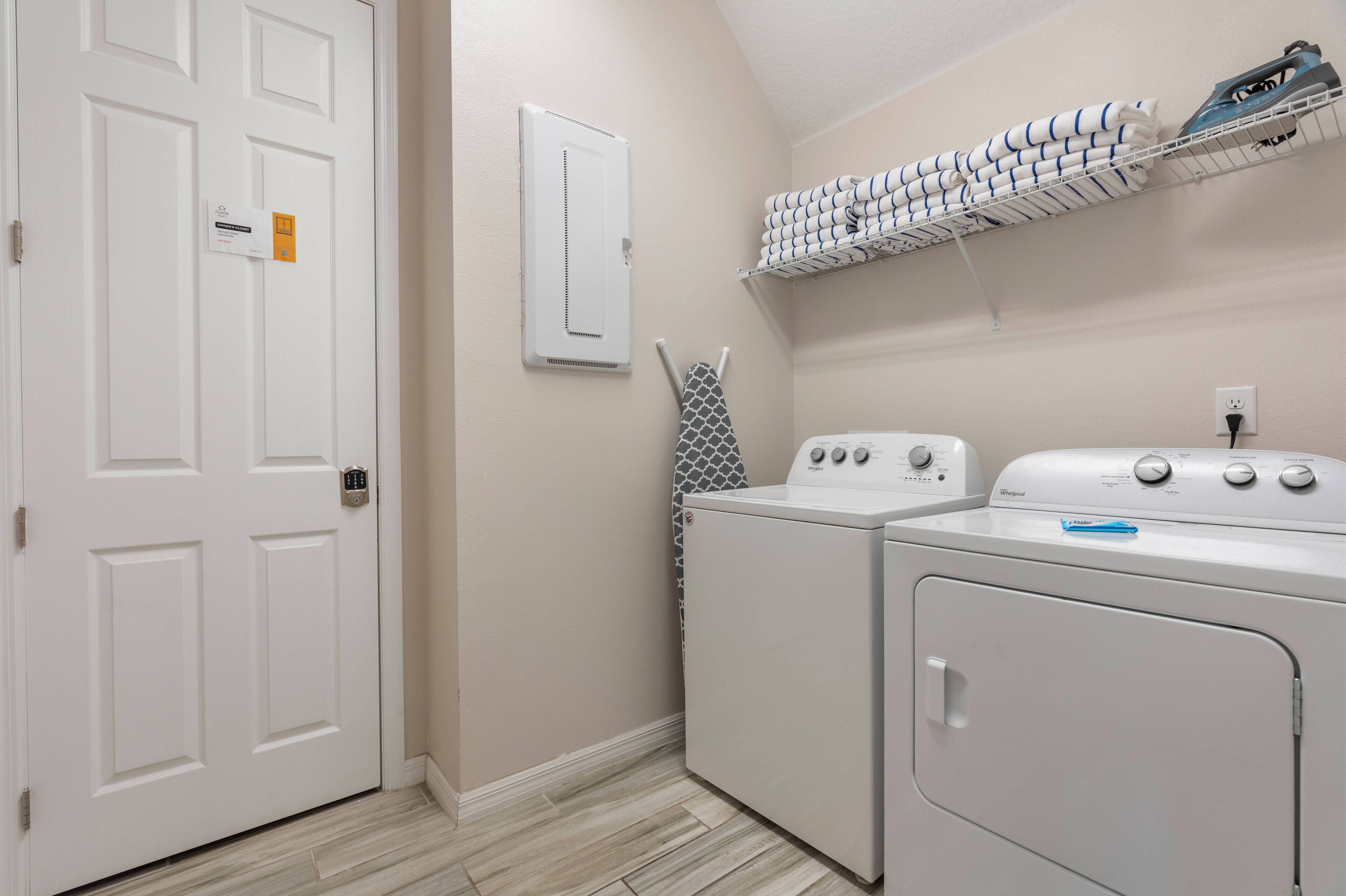 Une buanderie avec une porte blanche, un radiateur fixé au mur, un étendoir à linge empilable et un lave-linge et un sèche-linge à chargement frontal.
