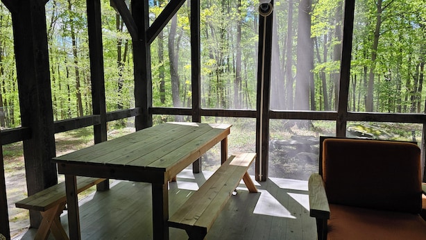 A wooden deck with picnic tables and benches, overlooking a forested area.
