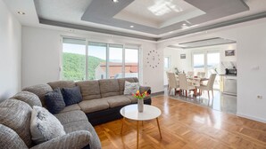 Amplia sala de estar con un sofá seccional grande, una mesa de centro redonda y vistas a un paisaje verde exuberante a través de amplios ventanales.