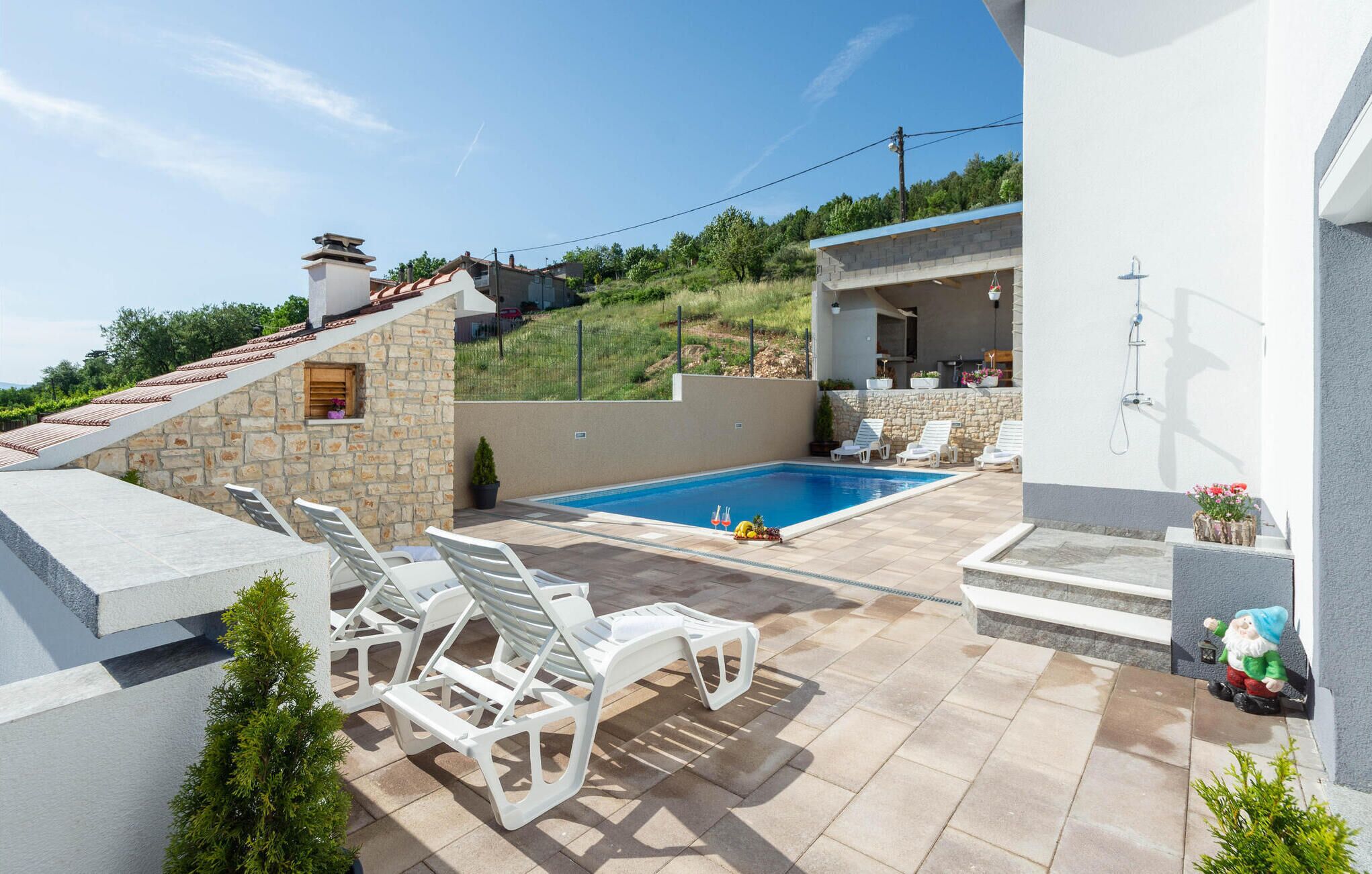 A modern outdoor pool area with stone walls, white lounge chairs, and a small deck.