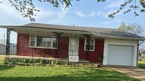 A single-story house with a red exterior, a covered porch, and a white garage door. - Cozy house/attached garage close to Lucas Oil Race Track and Pomme De Terre Lake (Wheatland)