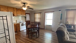 A spacious living room with a wooden floor, a dining area with a table and chairs, a kitchen with wooden cabinets and a stove, and a ceiling fan. - Cozy house/attached garage close to Lucas Oil Race Track and Pomme De Terre Lake (Wheatland)