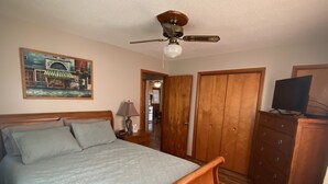 A bedroom with a wooden bed, a ceiling fan, a dresser, and a television. - Cozy house/attached garage close to Lucas Oil Race Track and Pomme De Terre Lake (Wheatland)