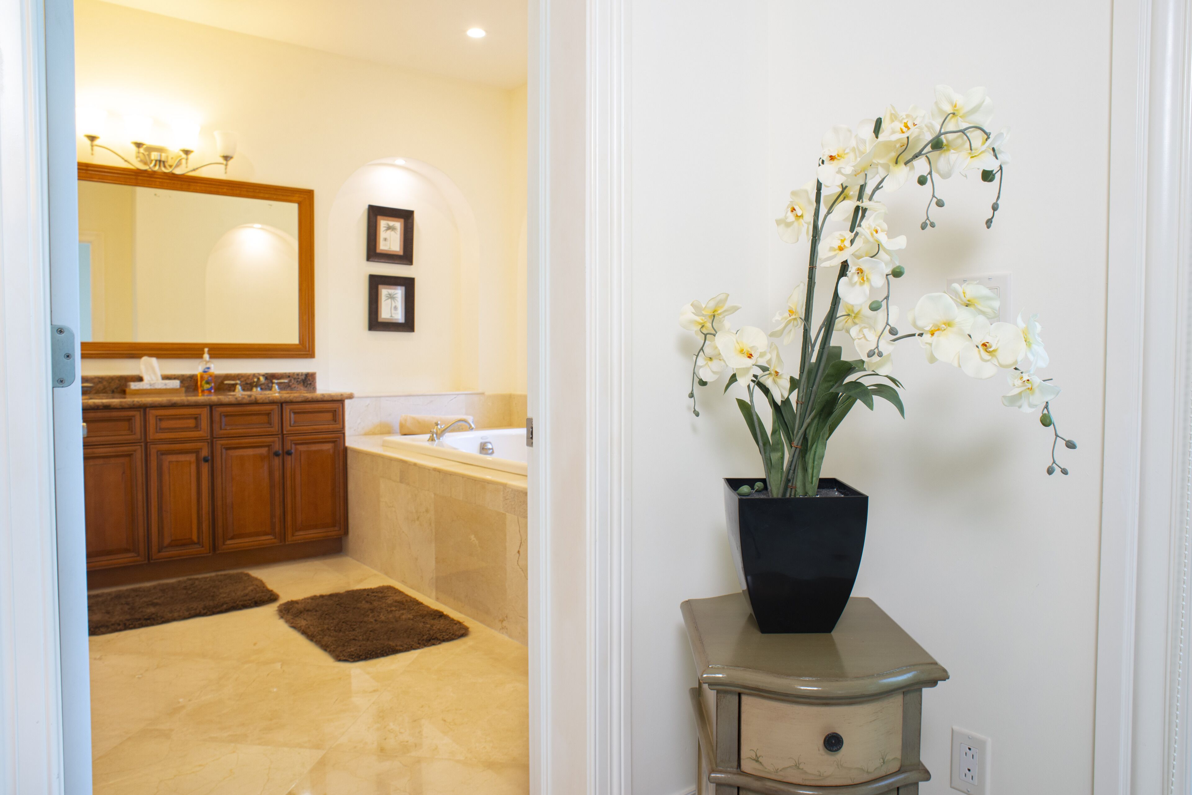 A bathroom with a large mirror, wooden cabinets, a bathtub, and a potted orchid.