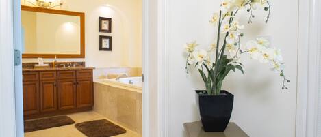 A bathroom with a large mirror, wooden cabinets, a bathtub, and a potted orchid.
