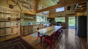 Ein rustikales Blockhaus-Interieur mit einem Holzesstisch, roten Stühlen, einer Küche mit Holzausbau und einem aufgehängten Tierkopf an der Decke.