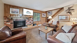 A cozy living room with a fireplace, leather sofas, a wooden staircase, and framed pictures on the walls. - Trapper 8 (West Yellowstone)