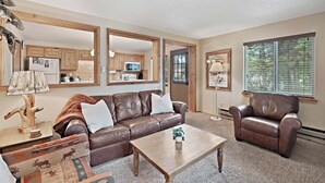 A living room with a brown leather sofa, a matching armchair, a wooden coffee table, and a large mirror. - Trapper 8 (West Yellowstone)