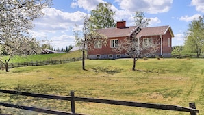 A red brick house with a sloped roof, surrounded by a wooden fence and trees.