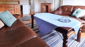 A living room with a brown leather sofa, a blue table, and a brick fireplace.