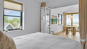 A modern bedroom with a large bed, a dining area with a table and chairs, and a view of the sea. - Cozy apartment in Kerteminde with WiFi (Kerteminde)