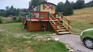 Eine Holzhütte mit Terrasse und Treppe, umgeben von einem Kiesweg und viel Grün.