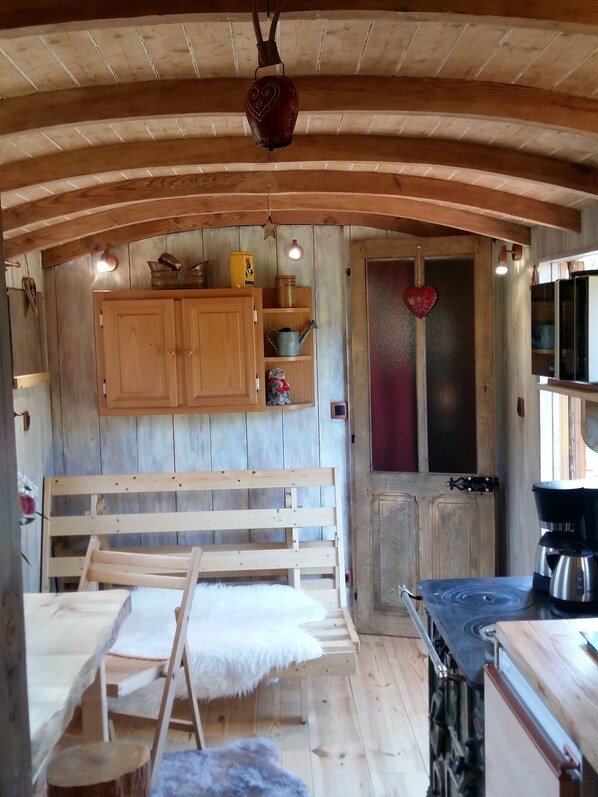 A rustic wooden interior with a bench, a small table, a dog, and a kitchen area with a stove.