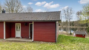 Une cabane en bois rouge, avec un toit en tuiles, une véranda et un petit abri situé à proximité.