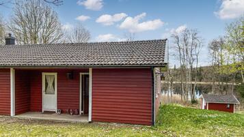 A red wooden cabin with a tiled roof, a porch, and a small shed nearby.