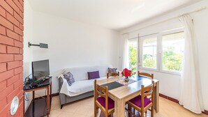 Une pièce comprenant un canapé, une table à manger avec des chaises, un téléviseur posé sur un meuble et une fenêtre avec des rideaux.