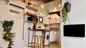 Un espace de vie compact comprenant un coin cuisine, un lave-linge, un téléviseur et un coin salon avec une table basse.