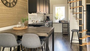Una cocina moderna con armarios de madera oscura, una mesa de comedor de madera con dos sillas grises, una cafetera y una estantería escalonada.