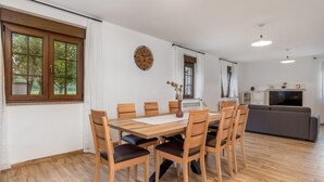 Ein Essbereich mit Holztisch und Stühlen, einer Uhr an der Wand und einem Sofa im Hintergrund.