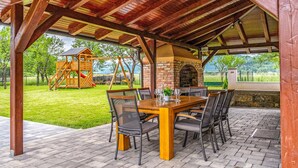 Eine Terrasse im Freien mit Holztisch und -stühlen, einem Kamin aus Ziegelsteinen und einer Schaukel im Hintergrund.