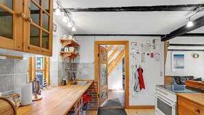 A kitchen with wooden cabinets, a built-in sink, and a stove. There is a wooden shelf above the sink and a door leading to another room.