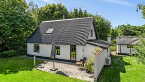 A two-story house with a sloped roof, a small attached garage, and a paved patio area with outdoor furniture.