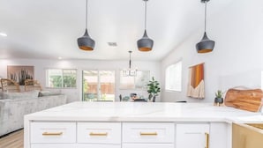 Una cocina moderna con armarios blancos, detalles dorados y luminarias colgantes.