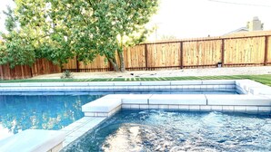 Una piscina con una valla de madera y un árbol al fondo.