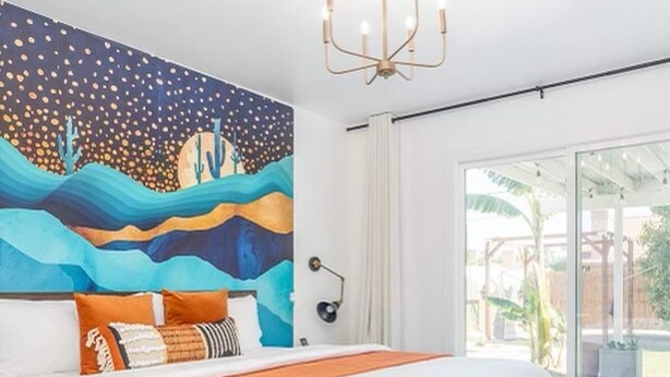 Un dormitorio con una cama grande, un mural en la pared, una lámpara de araña y vistas al exterior.