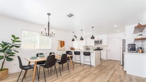 Una cocina moderna con armarios blancos, una isla central y taburetes negros.