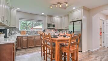 A modern kitchen with white cabinets, a granite countertop, a wooden dining table, and a stainless steel refrigerator.