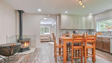 A modern kitchen with wooden cabinets, a dining table with chairs, a fireplace, and a view to a living area.