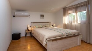 A bedroom with a wooden bed, bedside lamps, an air conditioner, and a window with curtains.